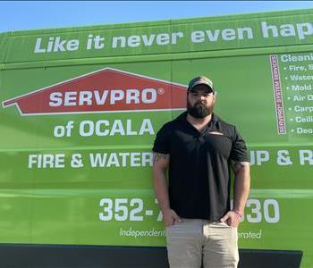 male employee standing against a green SERVPRO truck