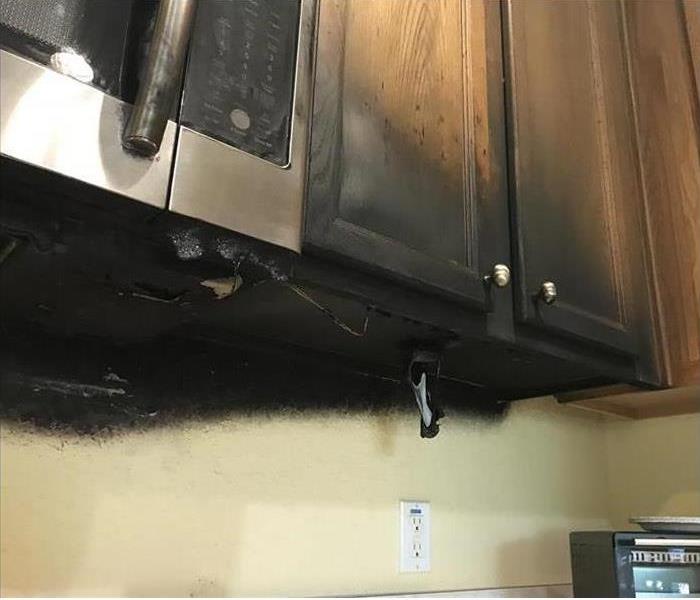 Kitchen fire caused by microwave under cabinet showing black soot and damage to cabinet