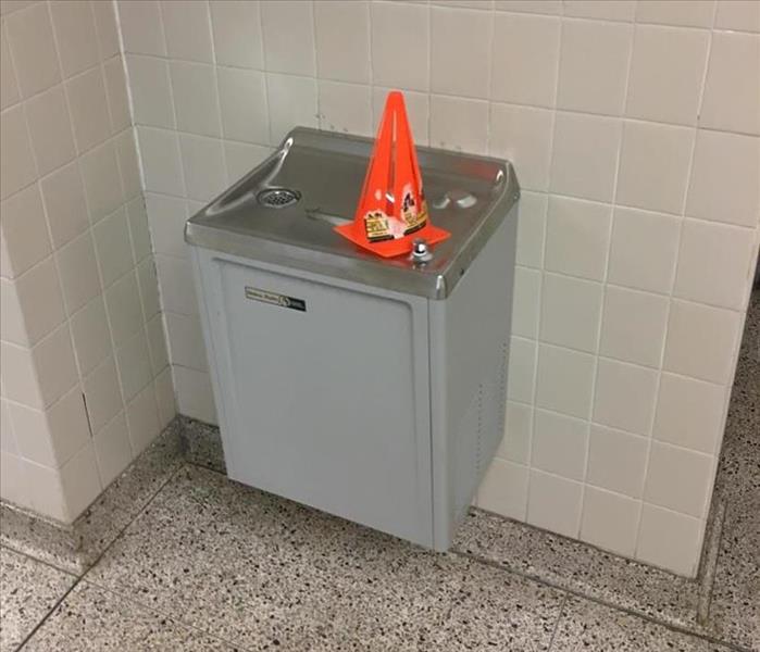 A orange cone on top of a broken drinking fountain